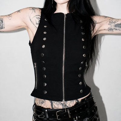 A black sleeveless studded vest with a front zipper, worn by a model with tattoos against a plain light gray background.