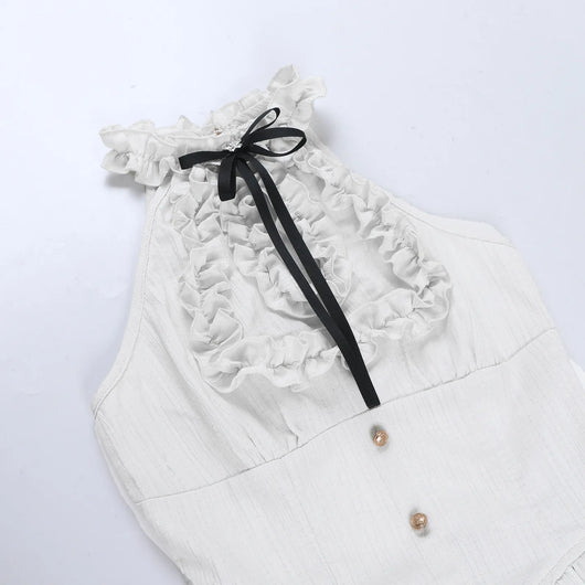 An off-white sleeveless top with a ruffled halter-style neckline, a black ribbon bow, and two small gold buttons, laid flat on a white background.