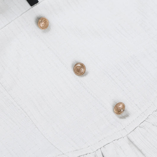 Close-up of a white textured fabric garment with three decorative gold buttons arranged diagonally.